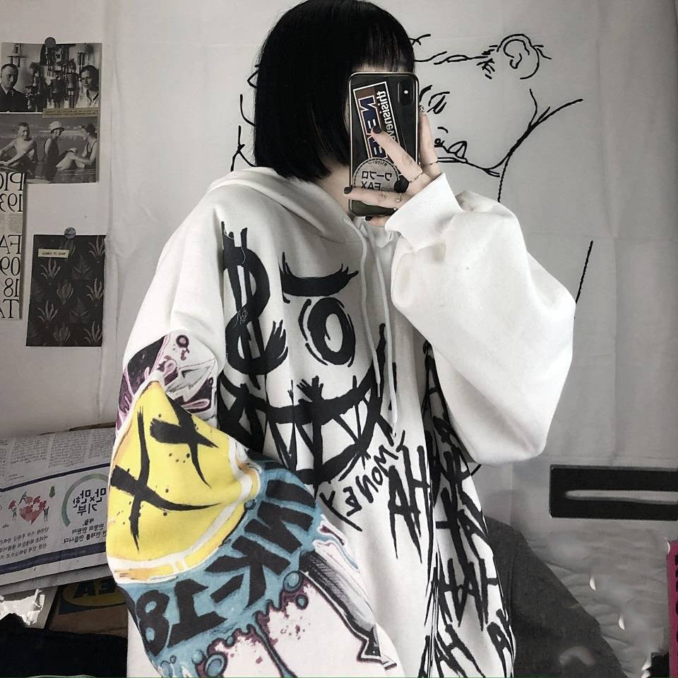 Person in weißem Graffiti-Hoodie mit buntem Design, hält Smartphone, urbaner Streetwear-Stil.