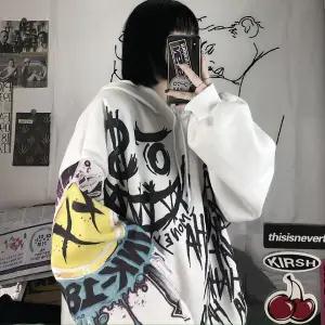 Person in weißem Hoodie mit Graffiti-Design, Smartphone, Streetwear, urbaner Stil.