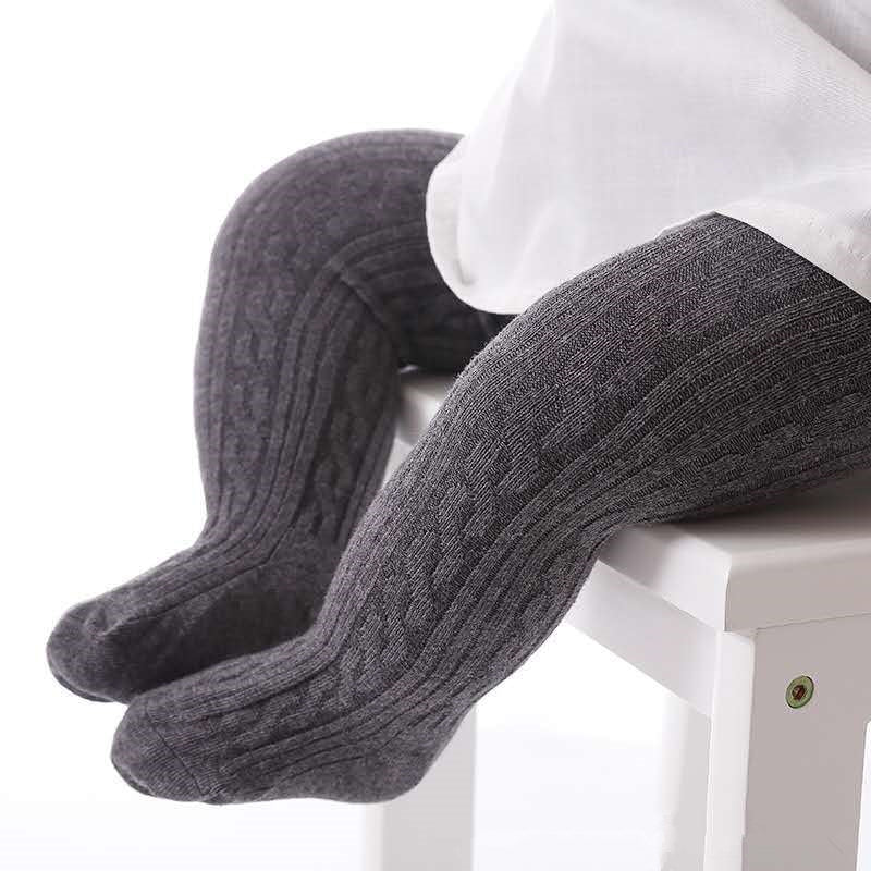 Graue Baby-Strumpfhose aus Baumwolle mit Zopfmuster auf weißem Stuhl.