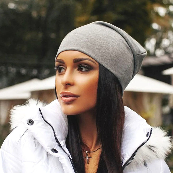 Frau mit grauer Beanie-Mütze und weißer Winterjacke, stilvolle Herbstmode im Freien.