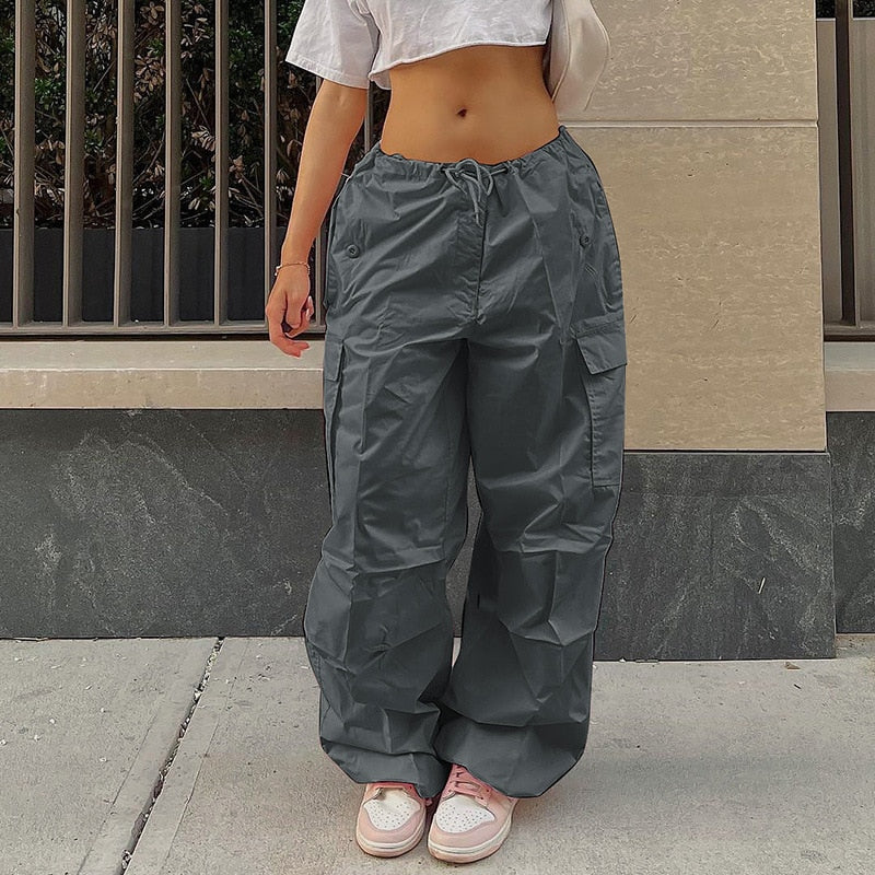 Frau in grauer Cargohose, weißem Crop-Top, rosa Sneakers, urbaner Hintergrund.