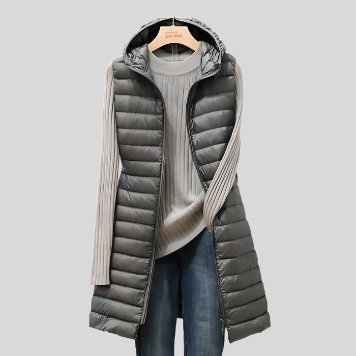 Graue Damen-Daunenweste mit Kapuze, gesteppte Optik, über grauem Pullover und Jeans.