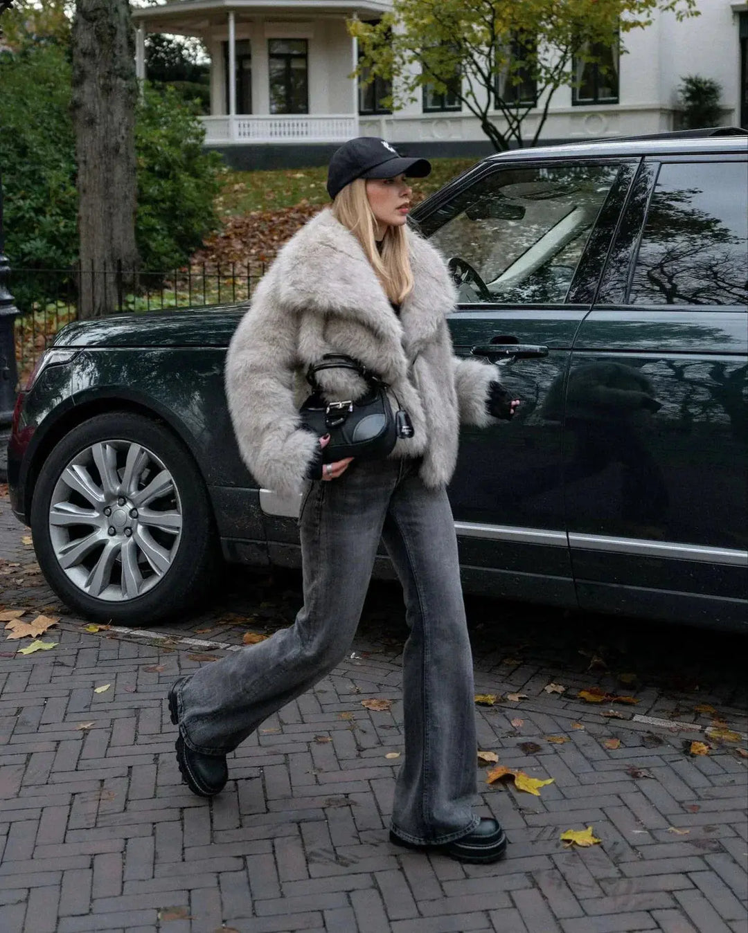 Frau in grauem Kunstpelzmantel und Jeans vor grünem SUV, Herbstszene, modisch, urban.
