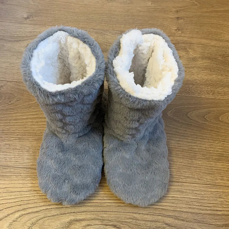 Graue Plüsch-Hausschuhe auf Holzboden, warmes Futter, gemütliche Winter-Fußbekleidung.