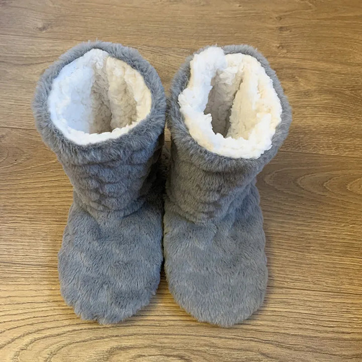 Graue Plüsch-Hausschuhe auf Holzboden, warmes Futter, gemütliche Winter-Fußbekleidung.