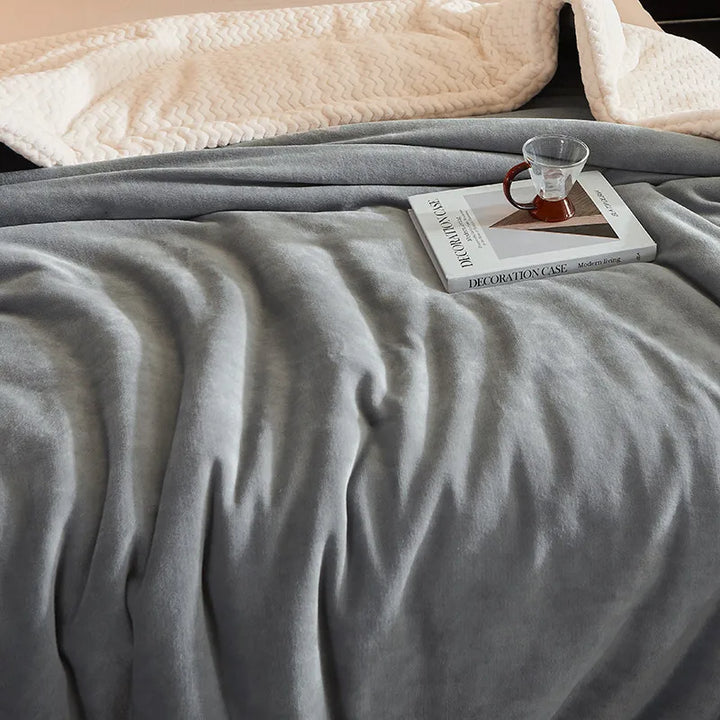 Graue Fleece-Decke auf Bett mit Buch und Teetasse, gemütliche Schlafzimmerdekoration.