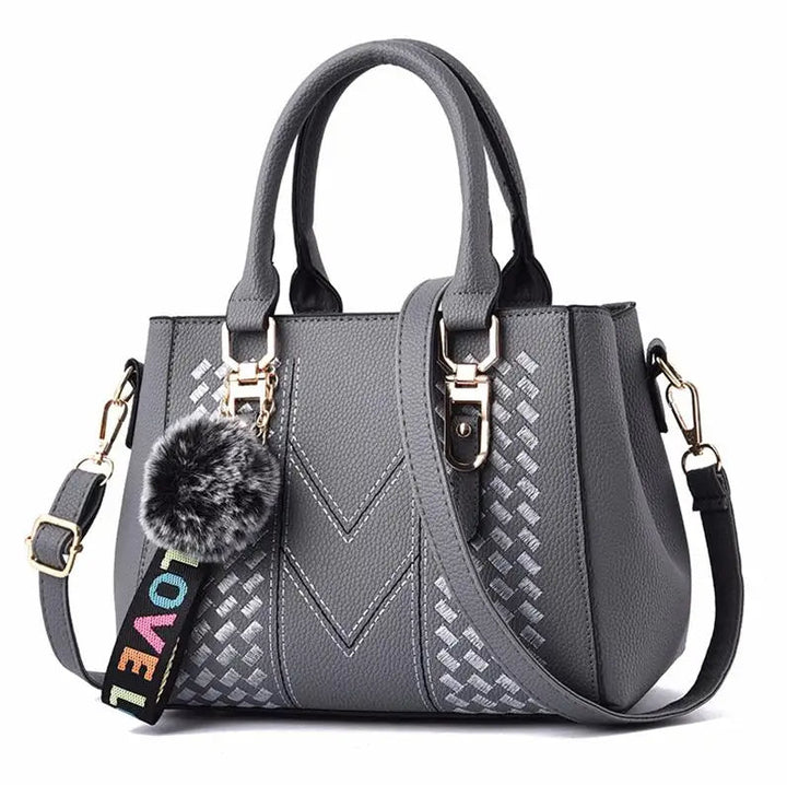 Graue Damenhandtasche mit Schulterriemen, Kunstleder, Pompon-Anhänger, modisches Design.