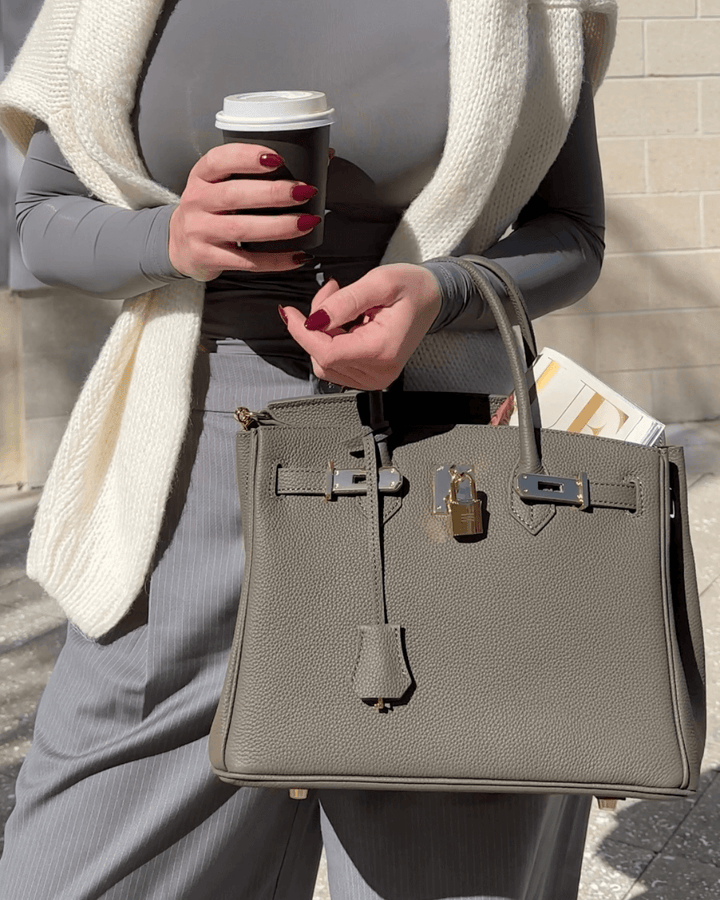 Frau mit grauer Lederhandtasche, Kaffeebecher und Zeitschrift, modisch, elegant, draußen.