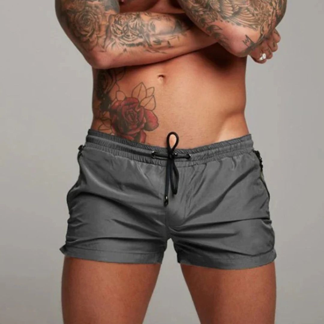 Mann in grauer Badehose mit Tattoos auf Oberkörper, sportlich, modisch, Strandmode.