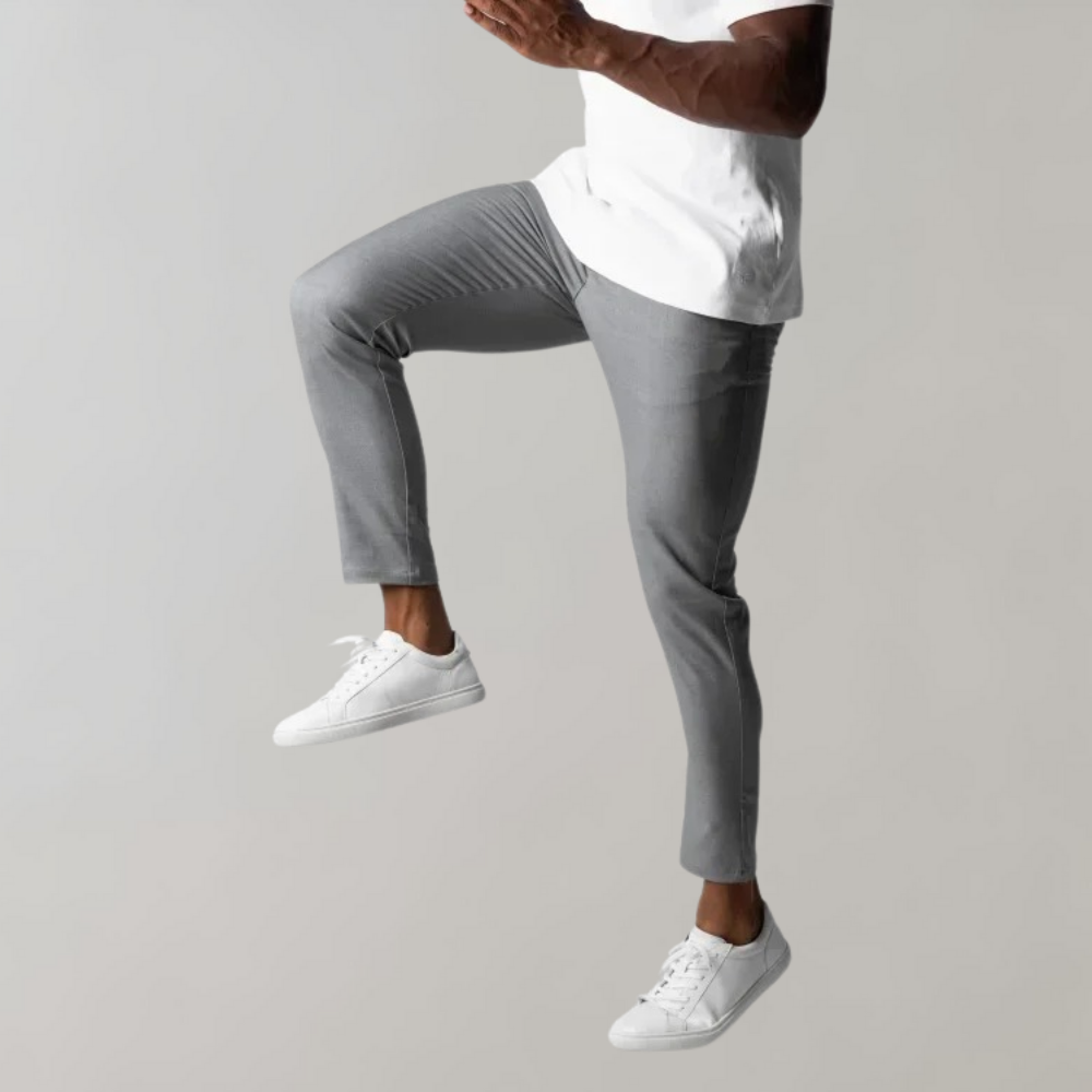 Mann in grauer Hose und weißen Sneakers, springend, vor grauem Hintergrund.