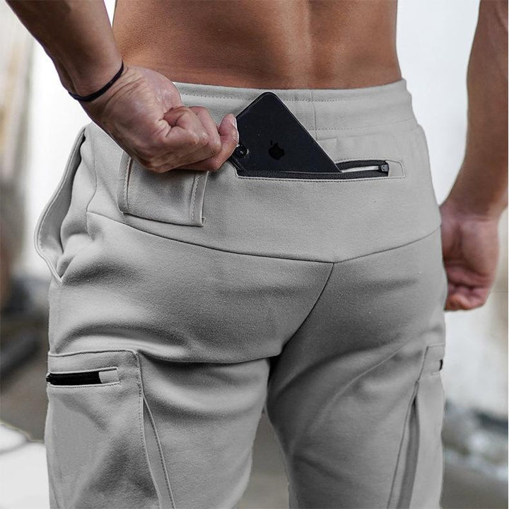 Mann in grauer Jogginghose steckt schwarzes Smartphone in Gesäßtasche, sportliche Freizeitkleidung.