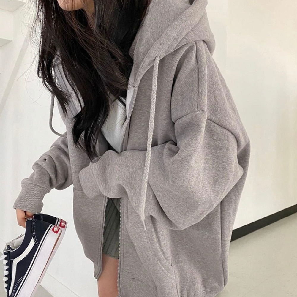 Frau in grauem Oversize-Hoodie, hält schwarze Sneaker, lässiger Streetwear-Look.