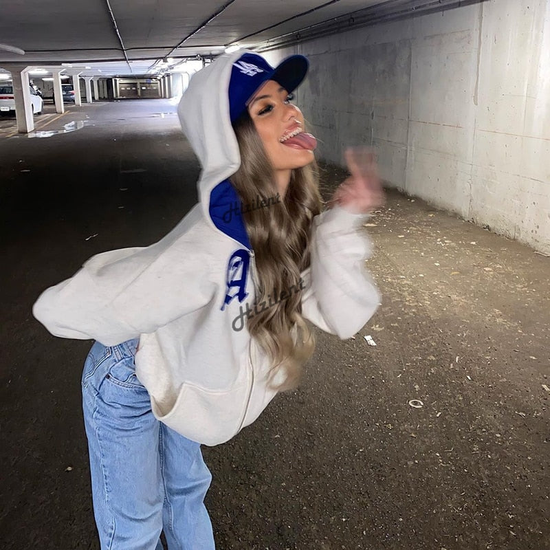Frau in weißem Hoodie und blauer Kappe posiert in Tiefgarage, lässiger Streetwear-Look.