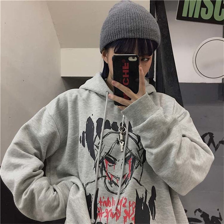 Person in grauem Hoodie mit grafischem Design, grauer Mütze, hält Smartphone, urbaner Stil.
