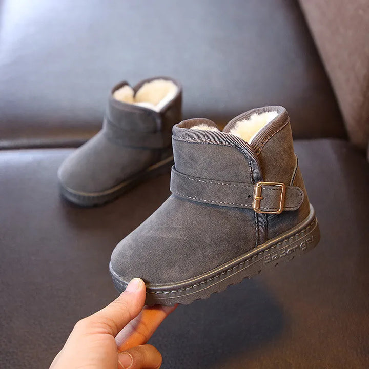 Graue Kinder-Winterstiefel aus Wildleder mit Schnalle und Fellfutter auf Ledersofa.