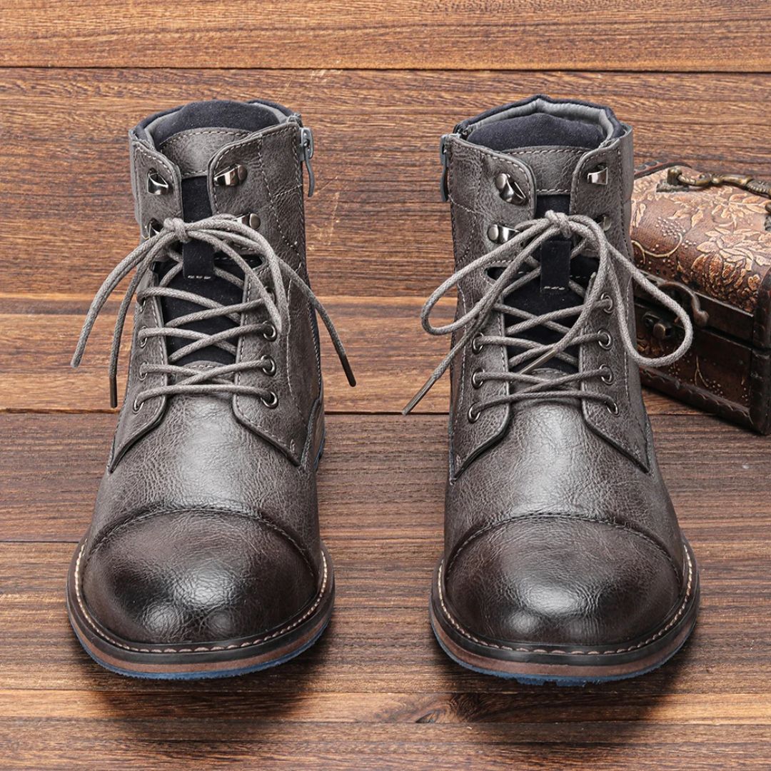 Graue Herrenstiefel aus Leder mit Schnürung auf Holzhintergrund.