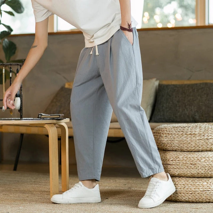 Mann in grauer Baumwollhose, weißem T-Shirt und Sneakers in modernem Wohnzimmer.