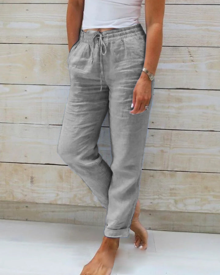 Frau trägt graue Leinenhose, lässig, mit Taschen, vor Holzwand, Sommermode.