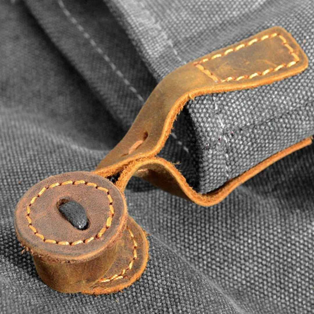 Graue Stofftasche mit braunem Lederknopf, robuste Nähte, modisches Accessoire.