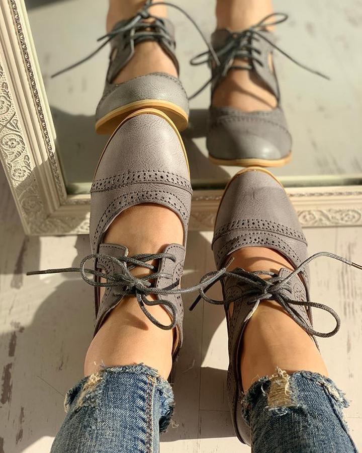 Graue Damen-Oxfordschuhe aus Leder, geschnürt, mit Lochmuster, vor einem Spiegel.