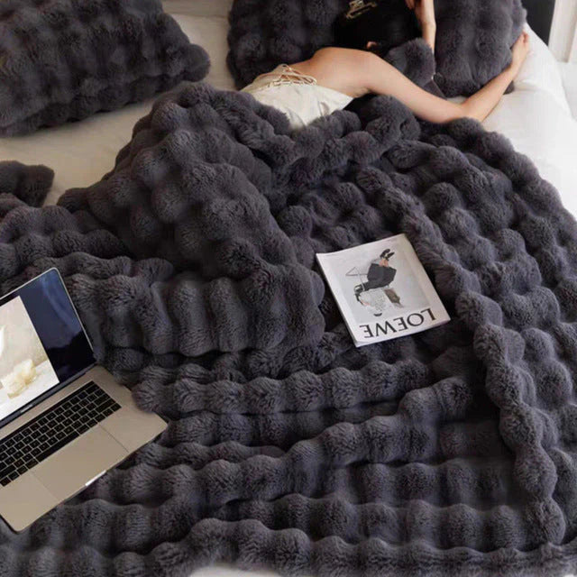 Graue, flauschige Decke auf Bett mit Laptop und Zeitschrift, gemütliches Schlafzimmer-Setup.