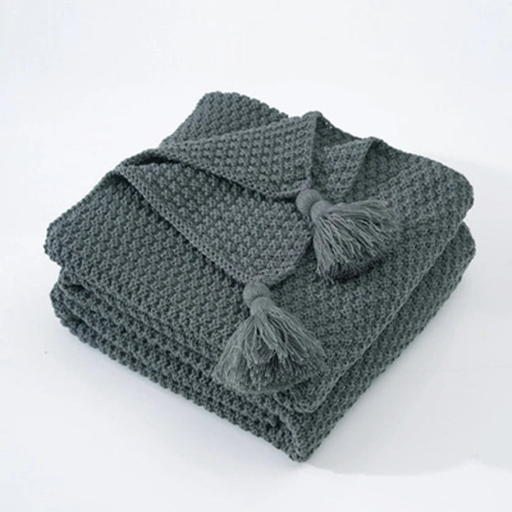 Graue Strickdecke mit Quasten, weiches Baumwollmaterial, ideal für Wohnzimmer oder Schlafzimmer.