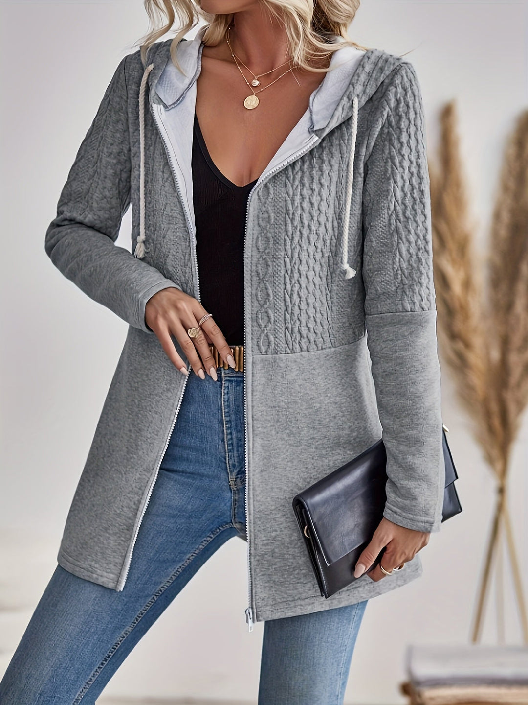 Frau in grauem Strickmantel mit Kapuze, schwarze Tasche, Jeans, lässiger Herbstlook.