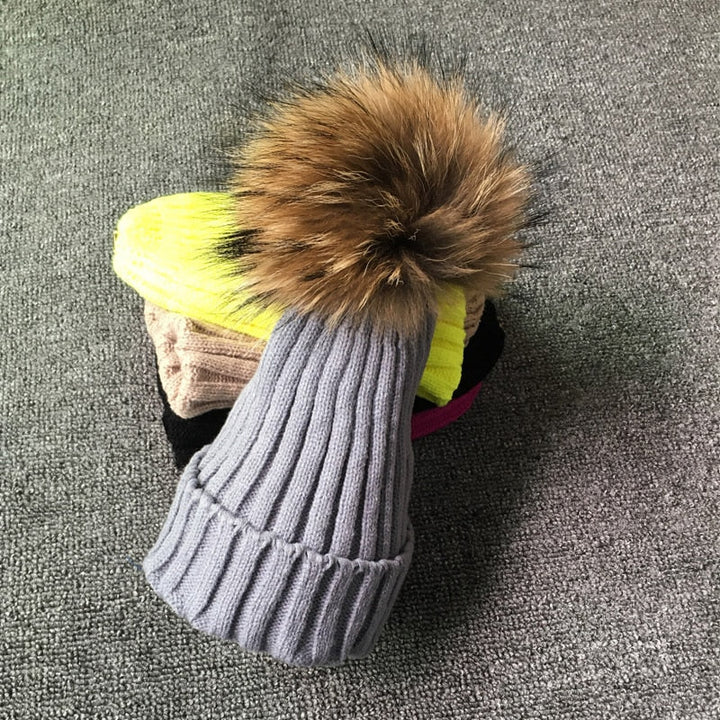 Graue Strickmütze mit Kunstfellbommel auf Teppich, Wintermode Accessoire.