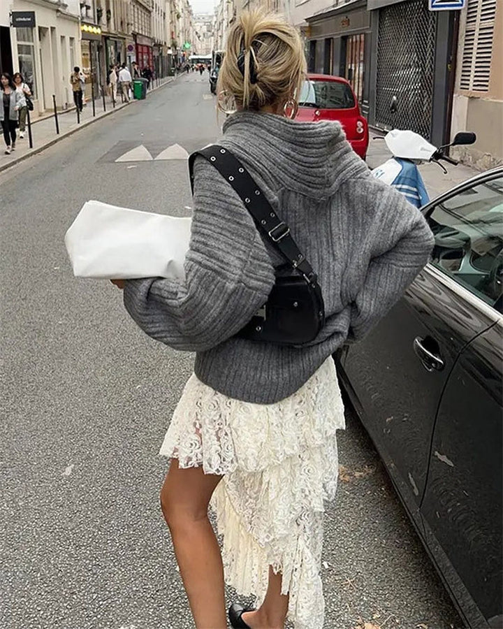 Frau in grauem Strickpullover und weißem Spitzenrock auf Stadtstraße, modisch, urban.