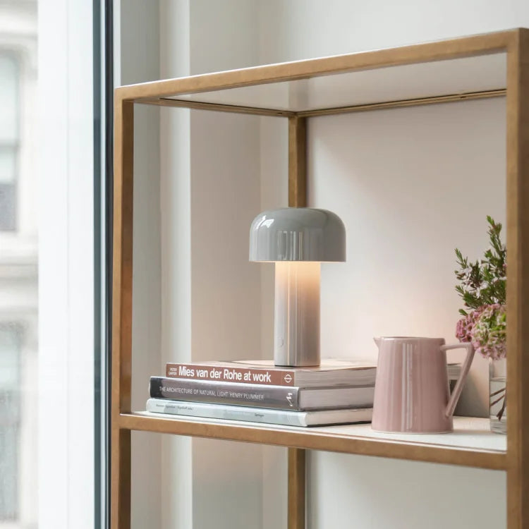 Graue Tischlampe auf Regal, neben Büchern und rosa Vase, modernes Innendesign.