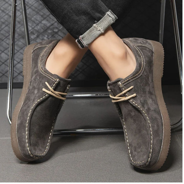 Graue Wildleder-Herrenschuhe mit Schnürung, lässig, bequem, modisch, auf grauem Boden.