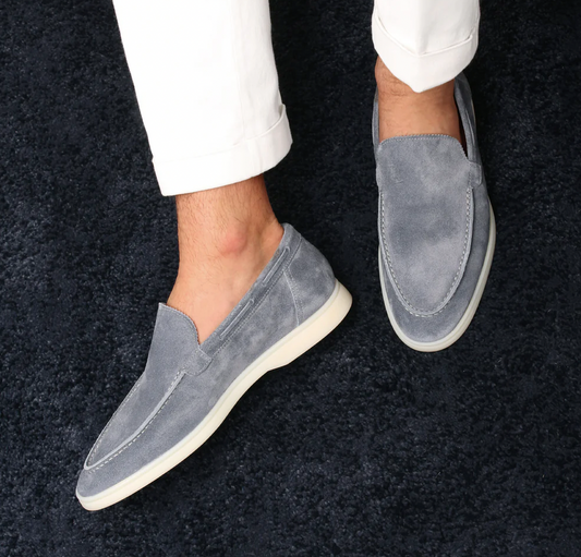Graue Wildleder-Slipper für Herren, elegante Freizeitschuhe, weiße Sohle, auf blauem Teppich.