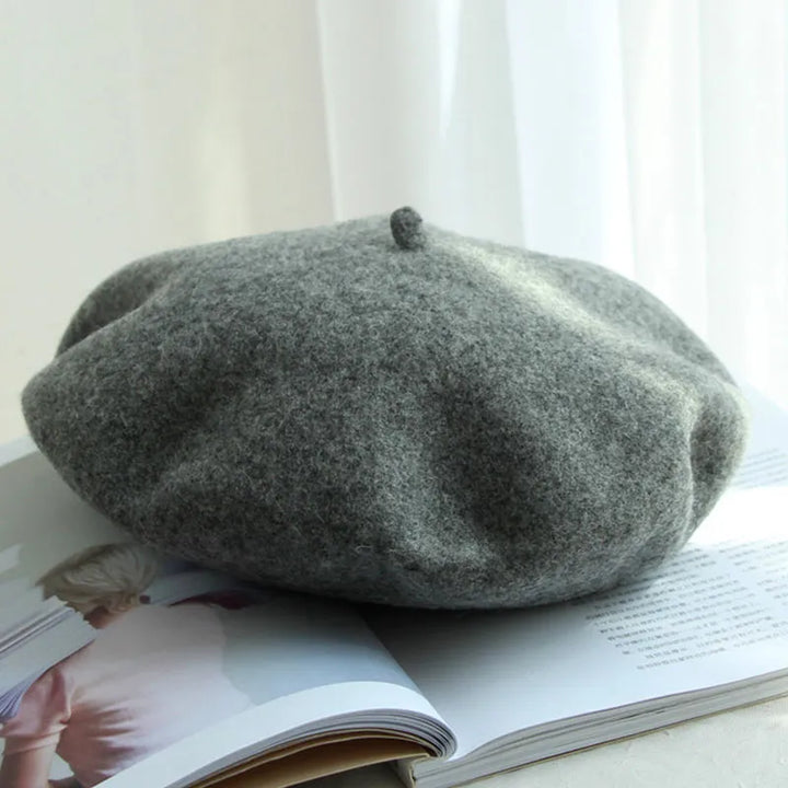 Graue Woll-Baskenmütze auf offenem Buch, stilvolles Accessoire, Herbstmode.