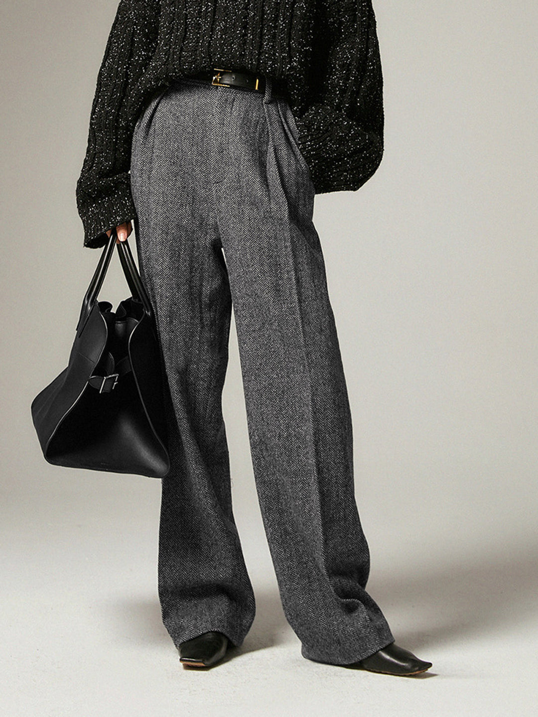 Frau in grauer Wollhose, schwarzem Pullover, hält schwarze Ledertasche, elegante Mode.