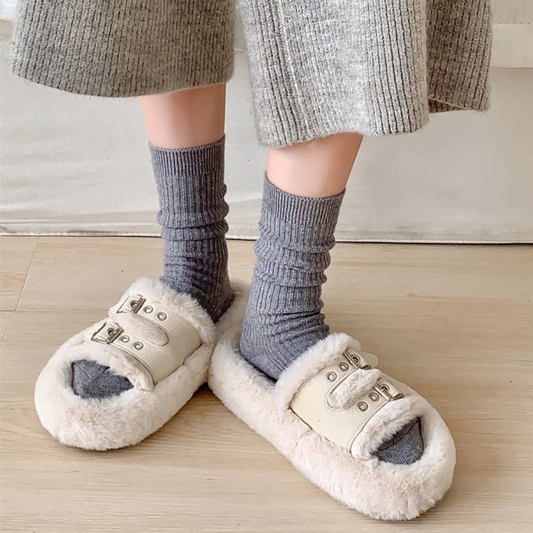 Graue Socken und flauschige Hausschuhe mit Schnallen auf Holzboden, gemütliche Wintermode.