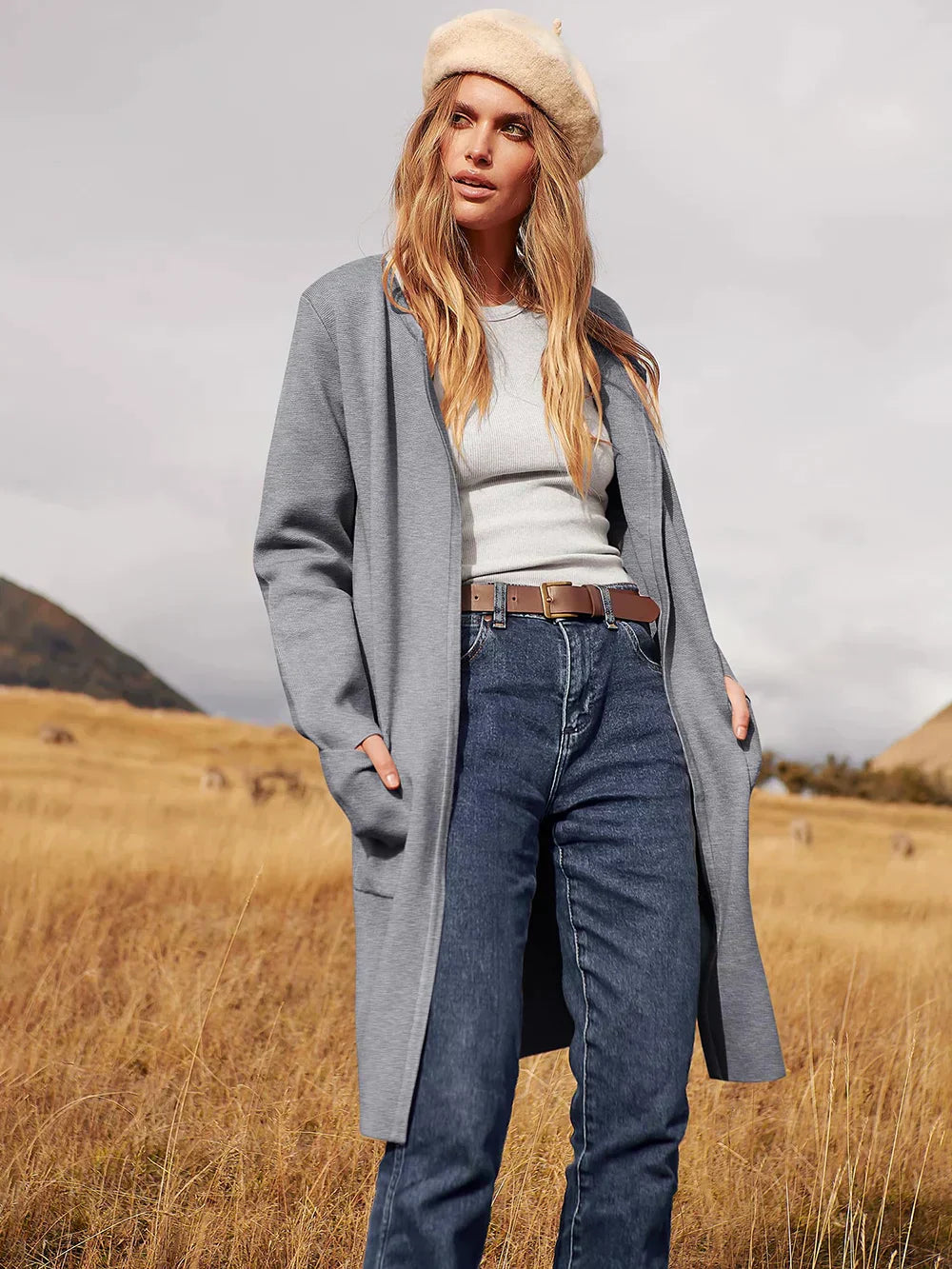 Frau in grauem Mantel und Jeans in Herbstlandschaft, beige Mütze, modisch, Outdoor-Bekleidung.