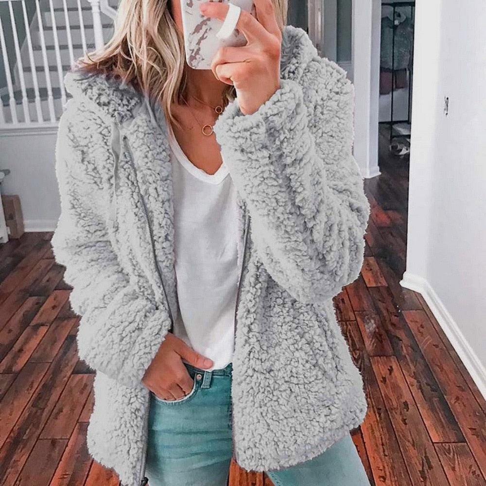 Frau in grauer Teddyjacke, weißem T-Shirt und Jeans, Selfie im Innenraum, modisch, gemütlich.