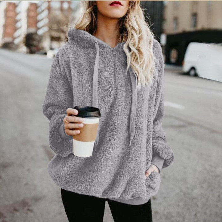 Frau in grauem Fleece-Hoodie mit Kaffeebecher, lässige Straßenmode, Herbstbekleidung.