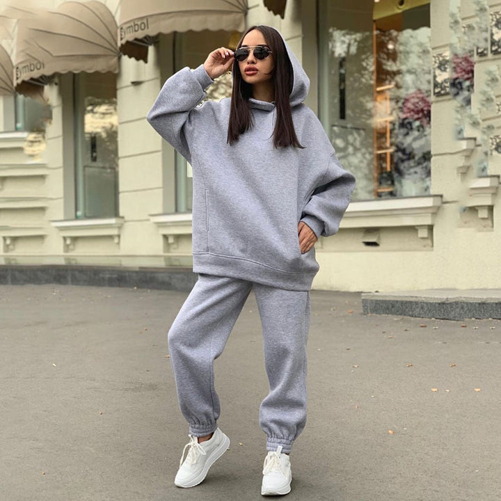 Frau in grauem Hoodie und Jogginghose, trägt Sonnenbrille, lässige Straßenmode, Herbst.