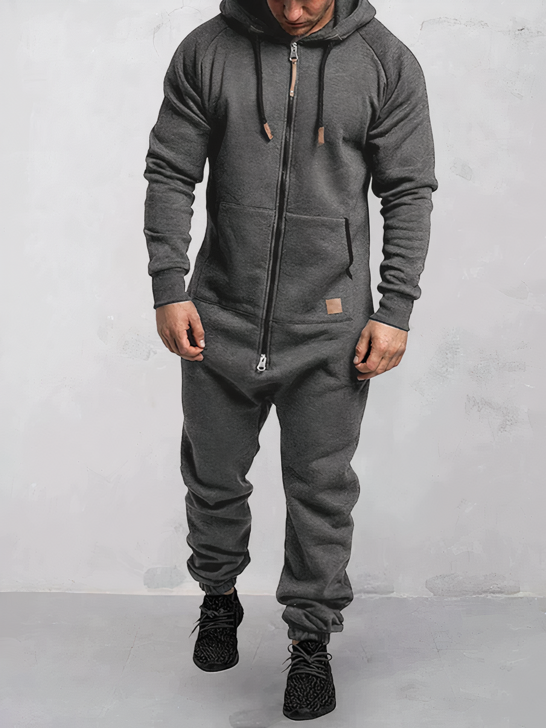 Mann in grauem Einteiler-Jumpsuit mit Kapuze, Reißverschluss, Freizeitmode, bequem, modern.
