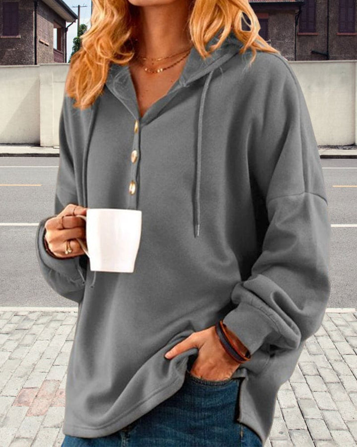 Frau in grauem Kapuzenpullover mit Kaffeetasse, lässige Mode, Herbstoutfit, Straße im Hintergrund.