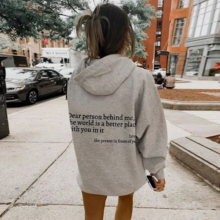 Frau in grauem Hoodie mit Aufschrift, Stadtstraße, Herbst, lässige Mode, Rückansicht.