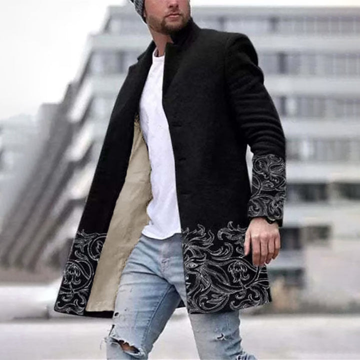 Mann in schwarzem Mantel mit grauem Muster, weiße T-Shirt, zerrissene Jeans, urbaner Hintergrund.