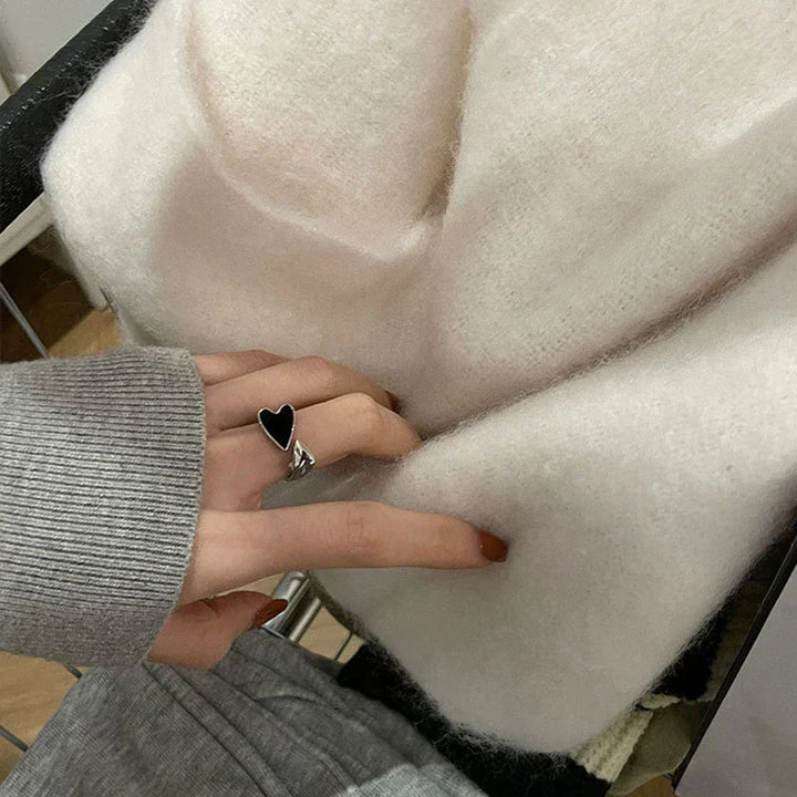 Damenhand mit Herzring berührt weiche, weiße Strickdecke aus Wolle im modernen Design.