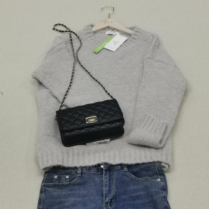 Grauer Strickpullover mit schwarzer Lederhandtasche und blauer Jeans auf beigem Hintergrund.