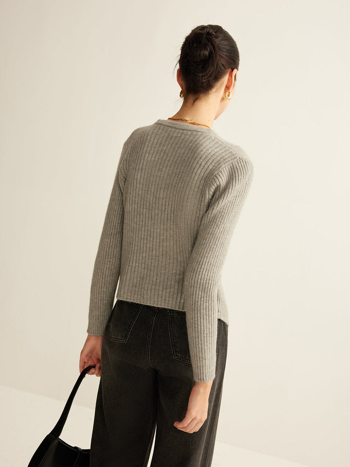 Frau in grauem Strickpullover und schwarzer Hose, hält schwarze Tasche, Rückansicht.