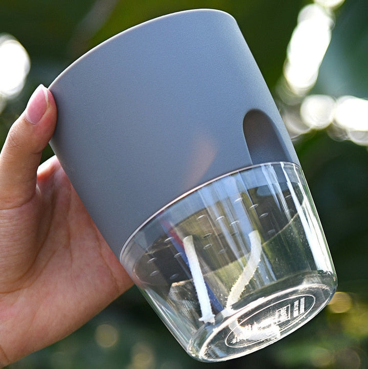 Grauer selbstbewässernder Blumentopf aus Kunststoff und Glas, handgehalten, für Zimmerpflanzen.