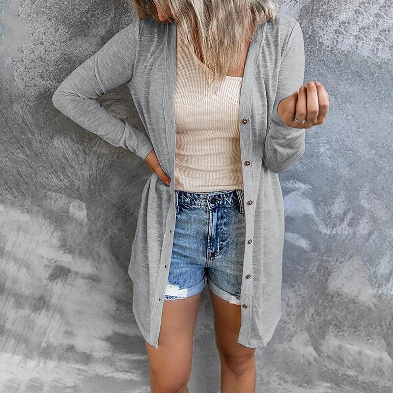 Frau in grauem Cardigan und Jeansshorts vor grauem Hintergrund.