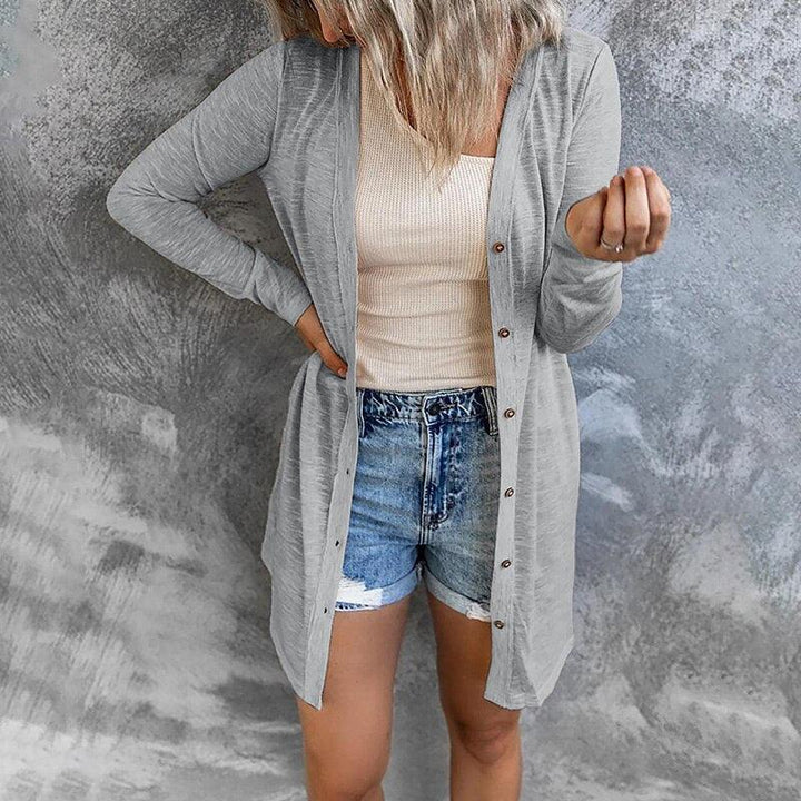 Frau in grauem Cardigan und Jeansshorts vor grauem Hintergrund.