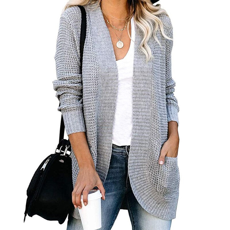 Frau in grauem Strickcardigan, weißem T-Shirt, Jeans, mit schwarzer Tasche und Kaffeebecher.